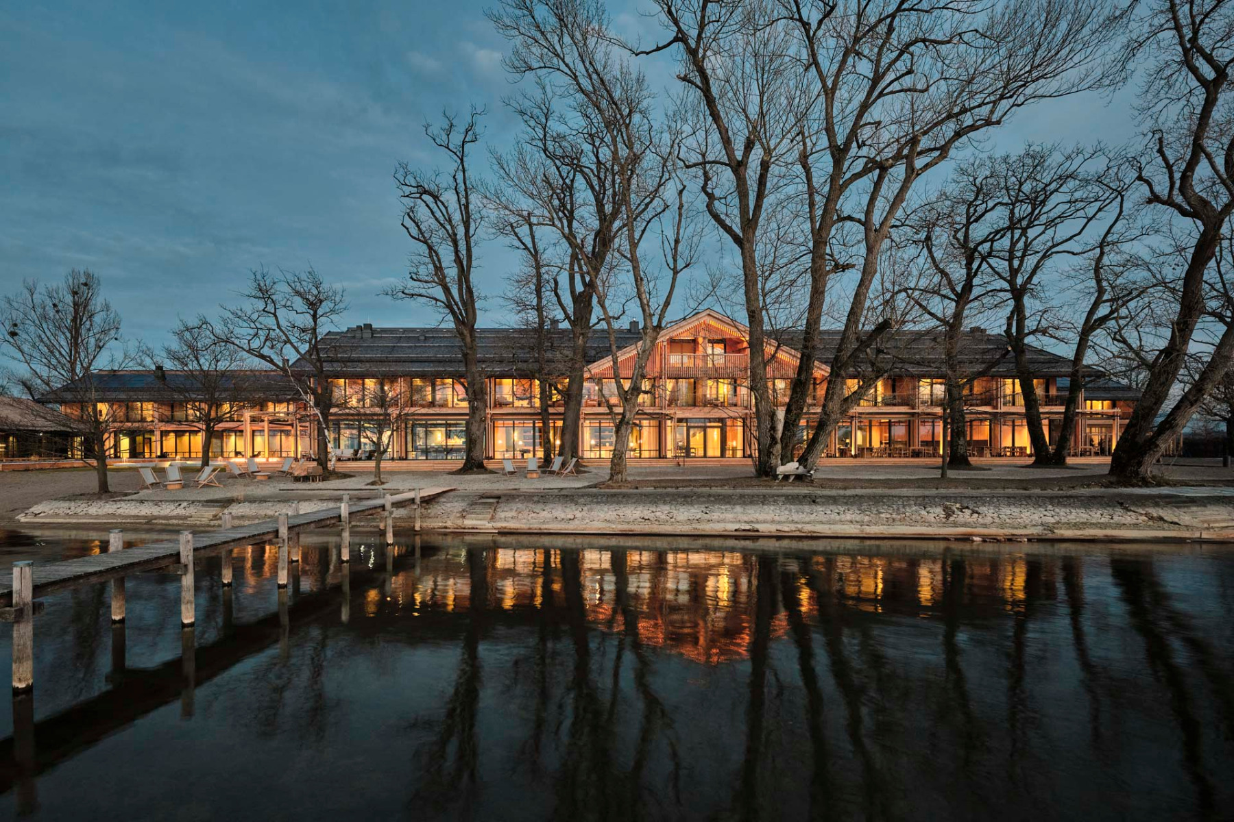 Die drei Holzgeb&auml;ude erstrecken sich entlang des Sees und sind durch Terrassen und verglaste Elemente verbunden. &copy; Elias Hassos
